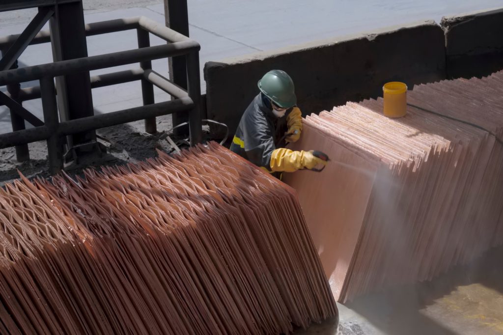Worker inspecting stacks of refined copper cathode sheets at a metals plant